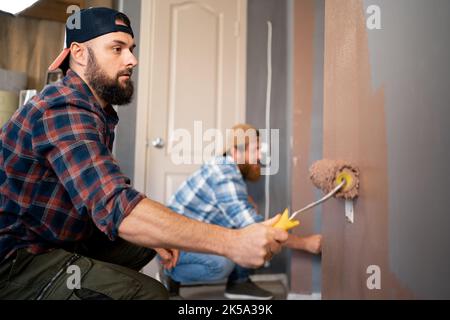 Young bearded workers painting wall in room with roller. repairs painting tools. repair, painting and home interior Stock Photo