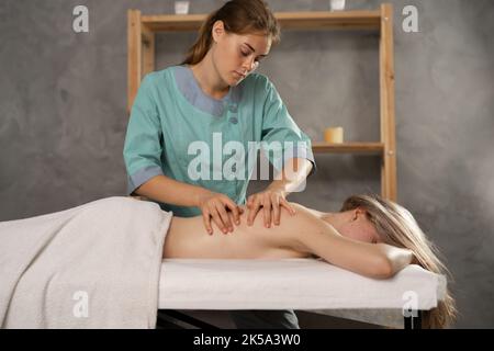 Beautiful young woman receiving relax massage in spa salon. Professional masseur doing therapeutic massage back. Massage therapy. Stock Photo