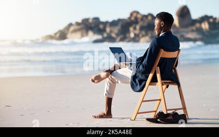 Beach, work and black man reading an email on a laptop with 5g internet while working by ocean. Relax, smile and happy African businessman doing Stock Photo