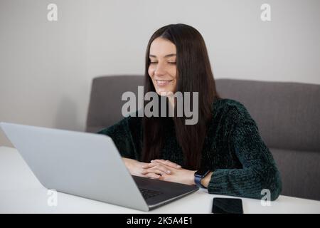 Happy brunette woman working on laptop at home. Cheerful white female person doing work on notebook computer Stock Photo