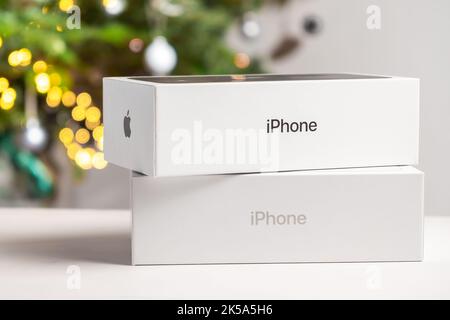 Apple boxes with iPhone against Christmas tree. Gifts for Christmas and New Year parties, October 2022, Prague, Czech Republic  Stock Photo