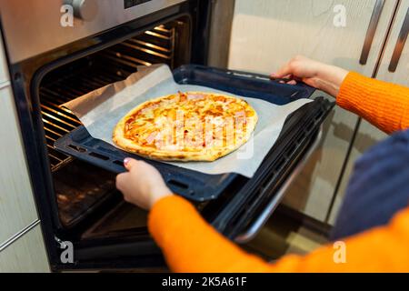 A woman taking out baking tray with delicious pizza from oven on kitchen Stock Photo