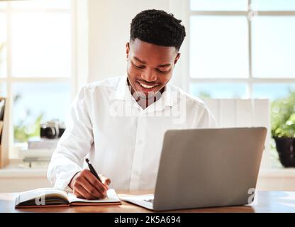 Internet, laptop and black man writing in notebook, happy freelance worker. African businessman with smile doing online research, taking notes for Stock Photo
