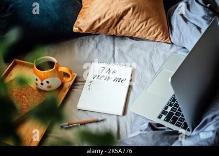 New Years Resolution. New me. Words New me in notebook near laptop and tea coffee cup at bad in home. Handwritten New me in notepad Stock Photo