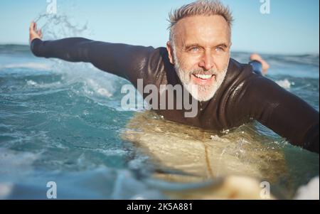 Beach, water and old man surfer swimming on a summer holiday vacation in retirement with freedom in Bali. Smile, ocean and senior surfing or body Stock Photo