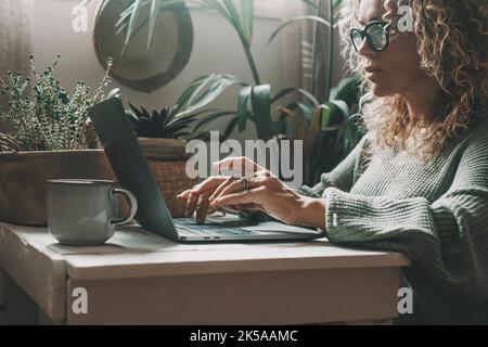 Professional woman working at home on laptop writing with concentrated expression. Modern female people using computer in indoor online leisure activi Stock Photo