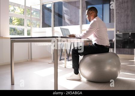 Correct Posture At Desk In Office Using Fitness Ball Stock Photo