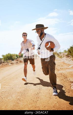 Football, friends and playing a game with man friends running on a dirt road or the dessert out in nature during the day. Running, fun and summer Stock Photo