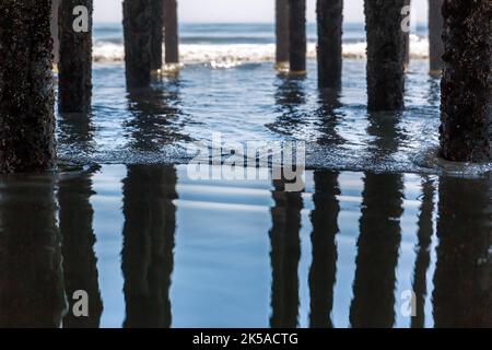 Selective focus on a gentle wave under the pier at Old Orchard Beach, Maine, USA. The pillars are reflected in the calm waters on a summer day. Stock Photo