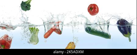 Mix of different vegetables splashing in water. Side panoramic view on white background. Stock Photo
