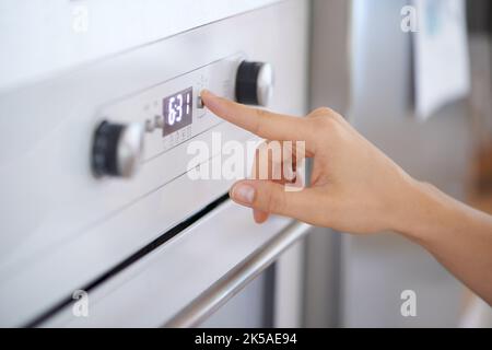 Putting on the power. Cropped view of a womans hand pushing a button on an oven. Stock Photo