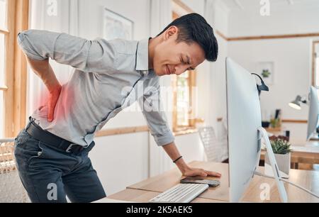 Businessman with back pain, muscle injury and burnout at office desk. Young frustrated man suffering from spinal inflammation, body discomfort or Stock Photo