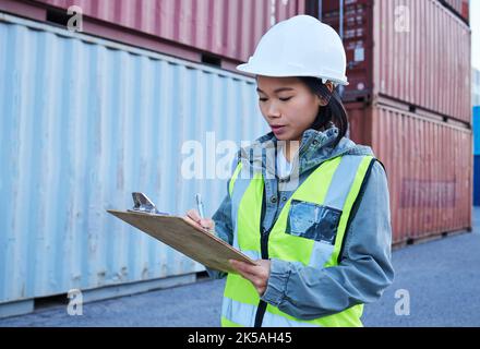 Logistics, shipping and asian woman engineer writing checklist report for inspection or delivery control of cargo containers at shipyard. Supply chain Stock Photo