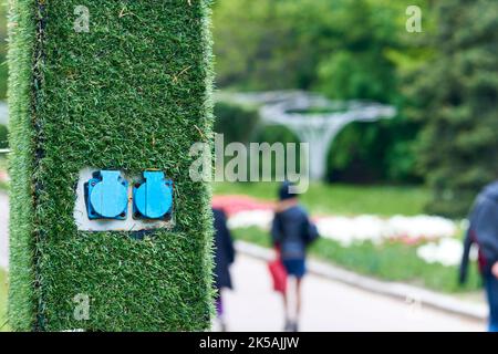 Electric sockets for charging on a pole with artificial green grass in the park Stock Photo