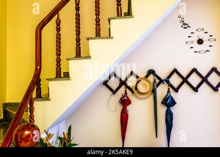 stairway up to the rooms with a coat rack with a hat and two umbrellas hanging on the wall. Stock Photo