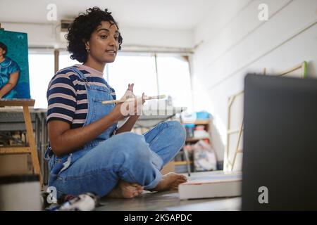 Woman artist, online class and laptop in art studio talking for video call, conference or zoom for teaching and education. Painter, internet and Stock Photo