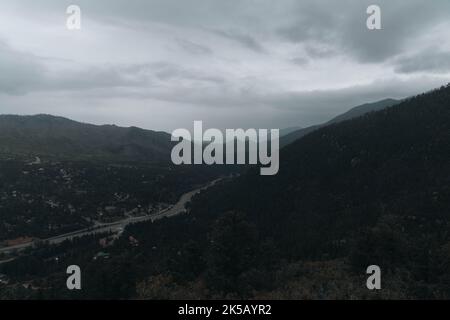 An aerial foggy view of a highway under pikes peak green mountains with trees in Colorado Stock Photo