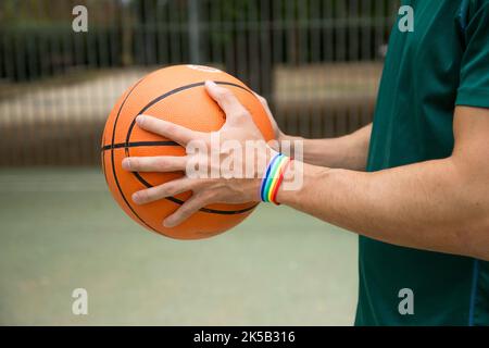 Cropped photo of an unrecognizable man holding a basketball ball wearing a rainbow bracelet Stock Photo