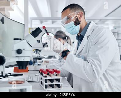 Scientist doing research for covid using a microscope and test tube in a lab. Healthcare worker in biotechnology, medicine and analytics testing Stock Photo