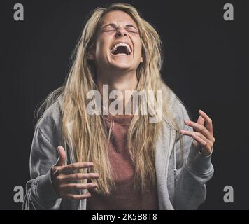 Mental health, crazy and bipolar woman laughing or shouting in dark studio for psychology, depression or identity problem. Drugs addiction Stock Photo