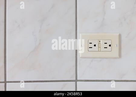 Electrical plug type B on the tiled wall in a bathroom. Stock Photo