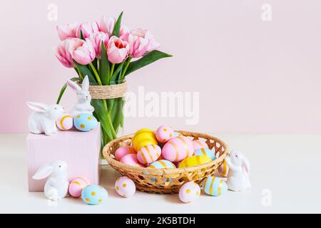 Easter and spring holiday greeting card concept. Pink tulips, easter bunnies with colorful eggs in basket. Painted Easter eggs in nest and tulips with Stock Photo