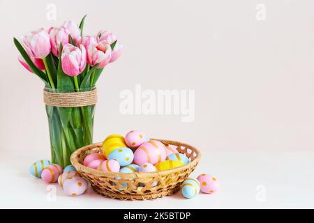 Easter and  spring holiday greeting card concept. Pink tulips with colorful eggs in basket. Painted Easter eggs in nest and tulips on color background Stock Photo