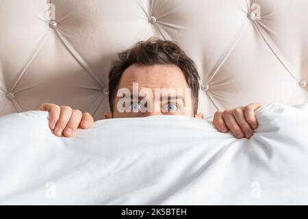Caucasian young man hiding in bed under the blanket at home. He is stressed and tries run away from problems. Stock Photo