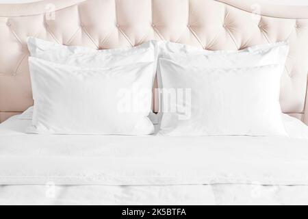 Bedroom with bed and white bedding White pillows, duvet and duvet case on bed with beige headboard.  Bed with clean white pillows and bed sheets in be Stock Photo