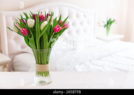 Bedroom in soft light colors. Vase of colorful tulips in light cozy bedroom interior. Home interior with pink tulips in a vase on a light bedroom back Stock Photo
