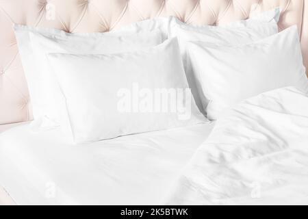 Bedroom with bed and white bedding White pillows, duvet and duvet case on bed with beige headboard.  Bed with clean white pillows and bed sheets in be Stock Photo