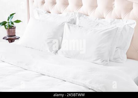 Bedroom with bed, white bedding, and bedside table. White pillows, duvet and duvet case on bed with beige headboard.  Bed with clean white pillows and Stock Photo