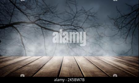 Spooky misty horror Halloween background with empty wooden planks, for product placement. Old wooden table and dead tree silhouette at night for Hallo Stock Photo