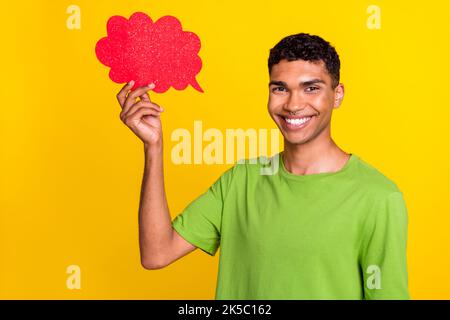 Portrait photo of young smiling attractive positive man wear green t-shirt hold red bubble cloud think idea plan isolated on yellow color background Stock Photo