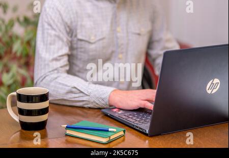 Man sitting at a desk typing on a laptop Stock Photo