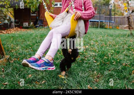 Bottom half of little girl swinging with toy stuffed monkey in yard Stock Photo