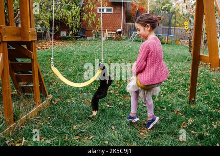 A little girl swings happily next to toy stuffed monkey in yard Stock Photo