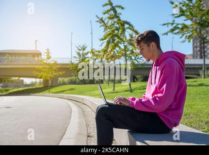 Young man sits on step, using laptop and looks on his screen. Stock Photo