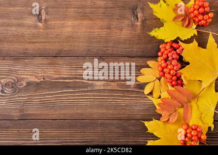 Autumn orange maple leaves and ripe rowan berries on a brown wooden table, top view. A place to copy. Autumn background. Stock Photo
