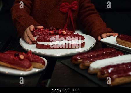 Little girl in red dress eats Traditional French dessert eclair with red chocolate and white filling in cafe Stock Photo