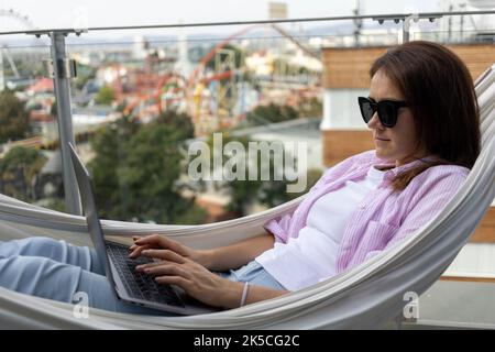 young woman freelancer working in hammock on terrace Stock Photo