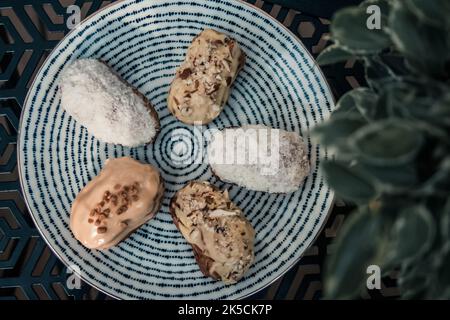 Mini eclairs with coconuts and hazelnuts on a plate in a cafe Stock Photo