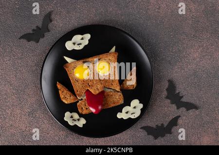 Fun Halloween monster sandwich with sausage, quail eggs, sweet pepper and cheese on black plate Stock Photo