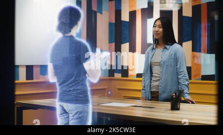 Asian woman talks on the call with her friend using augmented reality software. Hologram of her friend appears infront of her receiving the call. VFX special effects. Futuristic technology concept. Stock Photo