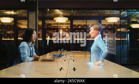 Video call chat conference of an asian woman using hologram technology. Conversing with a cartoon character avatar of young man. Advanced technology. VFX. Augmented reality. Stock Photo