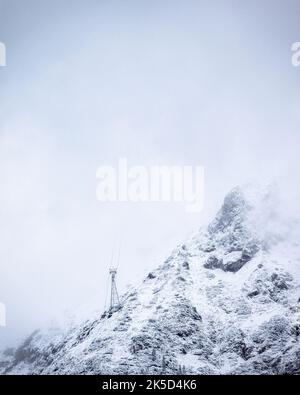 Cable car post on snow-covered mountain slope with cables disappearing in clouds. Mittenwald, Bavaria, Germany. Stock Photo