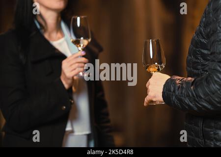Caucasian couple standing near a large wooden barrel in a wine cellar and tasting a quality white wine Stock Photo