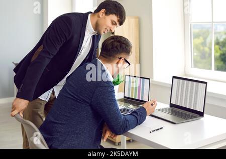 Smiling businesspeople using laptop, talking, communication, planning startup, working in office. Two business colleagues in meeting Stock Photo