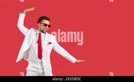 Happy funny man in white suit and sunglasses dancing isolated on red copy space background Stock Photo