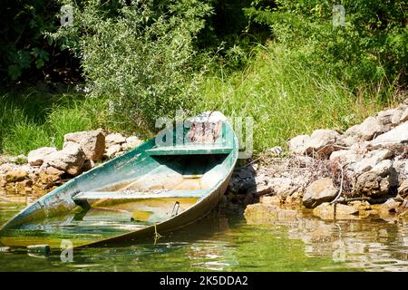 Old broken wooden boat under the water on the river coast. Traditional transportation Stock Photo